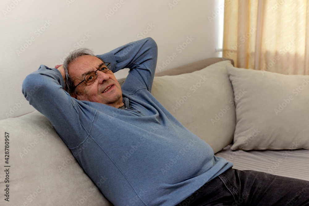 Retired man sitting on sofa, thinking about the future. Mindful old man daydream on cozy sofa in modern living room. Happy senior retired 70s grey haired man relaxing and enjoying peaceful lazy moment
