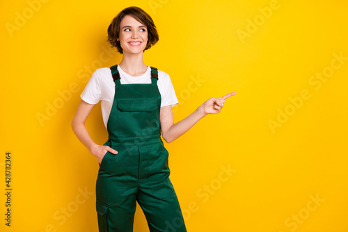 Photo of cheerful lady put arm in pocket look indicate finger empty space offer isolated on yellow color background