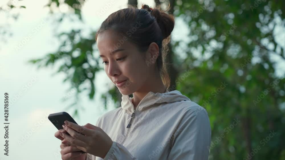 Asian sport woman typing on mobile phone with smile in the public park