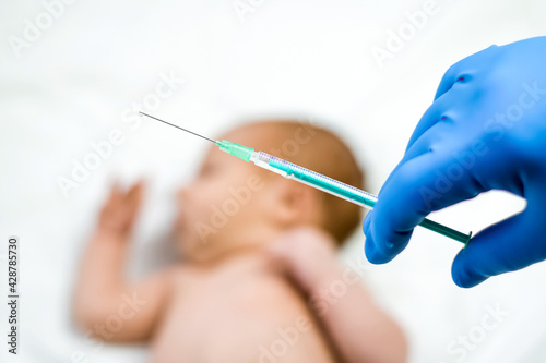 Pediatrician vaccinating newborn baby. Vaccine  Vaccination for infant child Soft focus Syringe in hands of a nurse and blurred background of infant baby on white. Doctor in blue gloves close up.