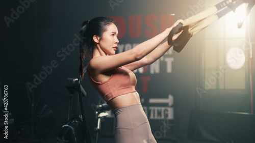 Young Sexy fit Asian woman in sportswear using TRX exercise equipment at the gym. Young strong lady with healthy lifestyle workout motivation
