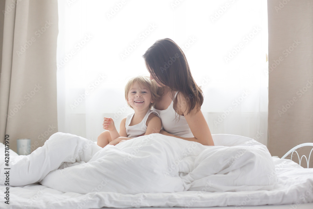 Beautiful blond child and his mother, playing at home in the morning in bed, smiling, laughing and having fun Beautiful blond child and his mother, playing at home in the morning in bed, smiling, laughing and having fun