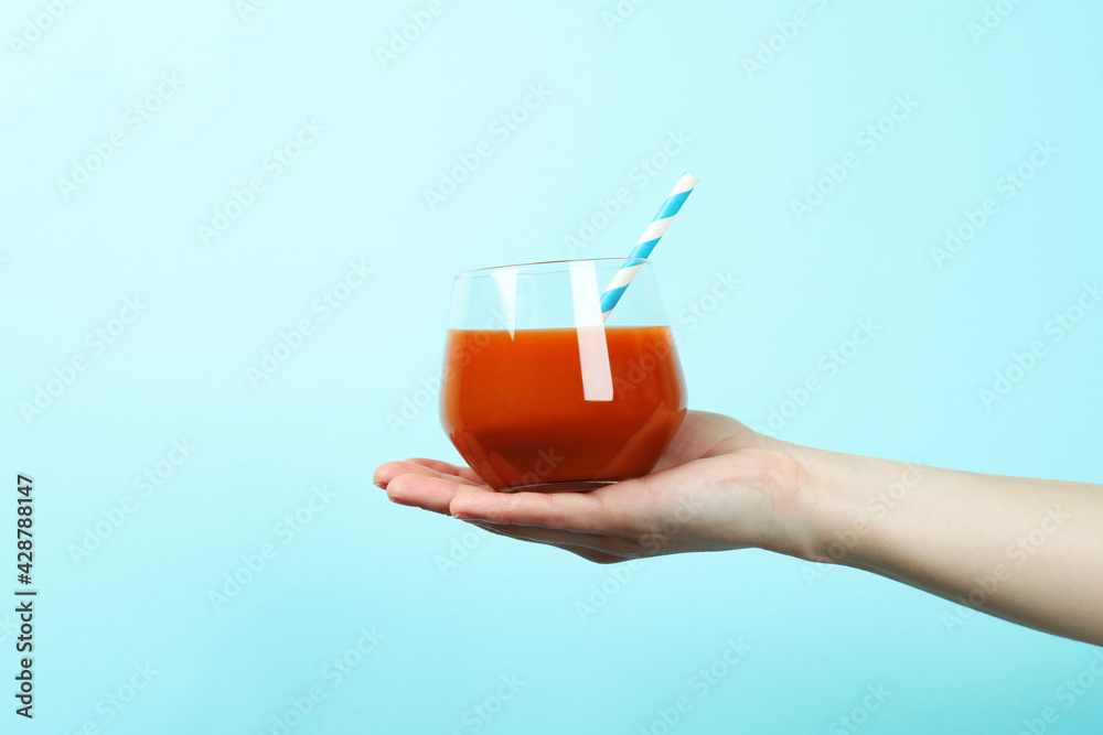 Female hand hold glass of juice on blue background Female hand hold glass of juice on blue background