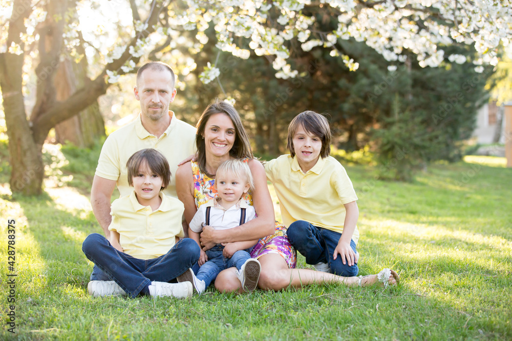 Beautiful family, mother, father and three kids, boys, having familly outdoors portrait taken on a sunny spring evening, beautiful blooming garden, sunset time Beautiful family, mother, father and three kids, boys, having familly outdoors portrait taken on a sunny spring evening, beautiful blooming garden, sunset time
