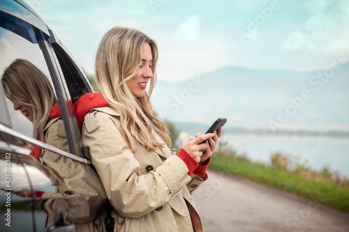 Stylish Woman calling and talking in smartphone, Girl with mobile phone standing near the car in sunny day.
