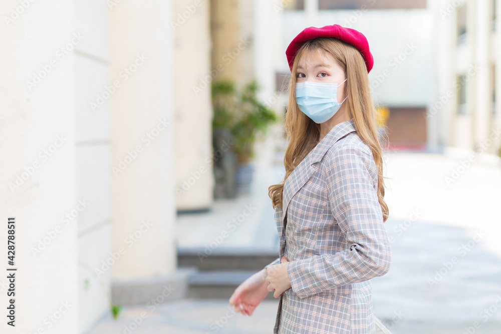 Asian woman in long bronze hair who wears grey suit and walks in the city and wearing medical face mask in new normal lifestyle.