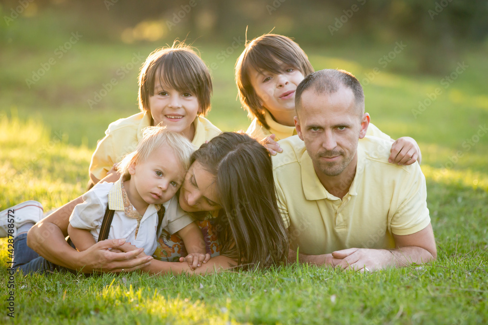 Beautiful family, mother, father and three kids, boys, having familly outdoors portrait taken on a sunny spring evening, beautiful blooming garden, sunset time