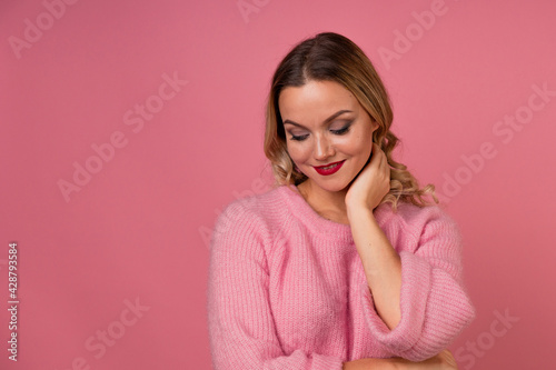 Young attractive woman in a warm pink sweater on a pink background,