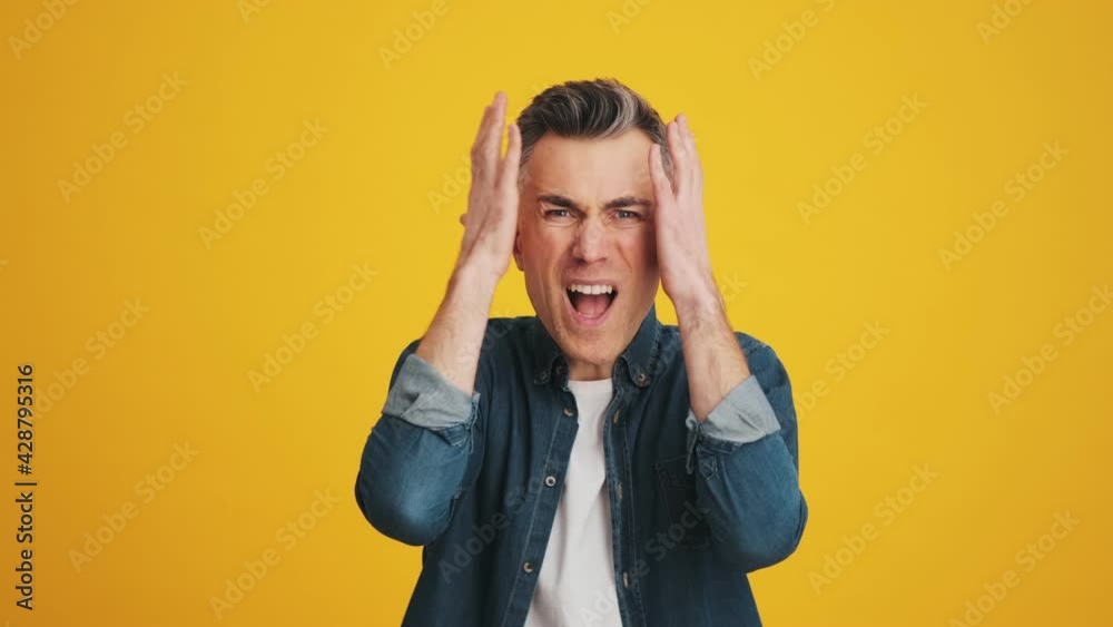 A surprised man saying what clutching his head with his hands while standing in the studio A surprised man saying what clutching his head with his hands while standing in the studio