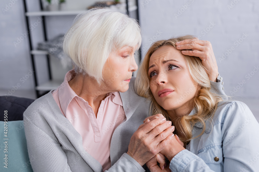 Elderly mother hugging displeased daughter at home Elderly mother hugging displeased daughter at home