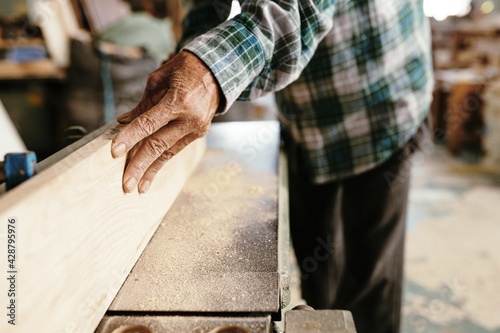 Close-up image of senior carpenter using bench top jointer to produce flat surface along boards length