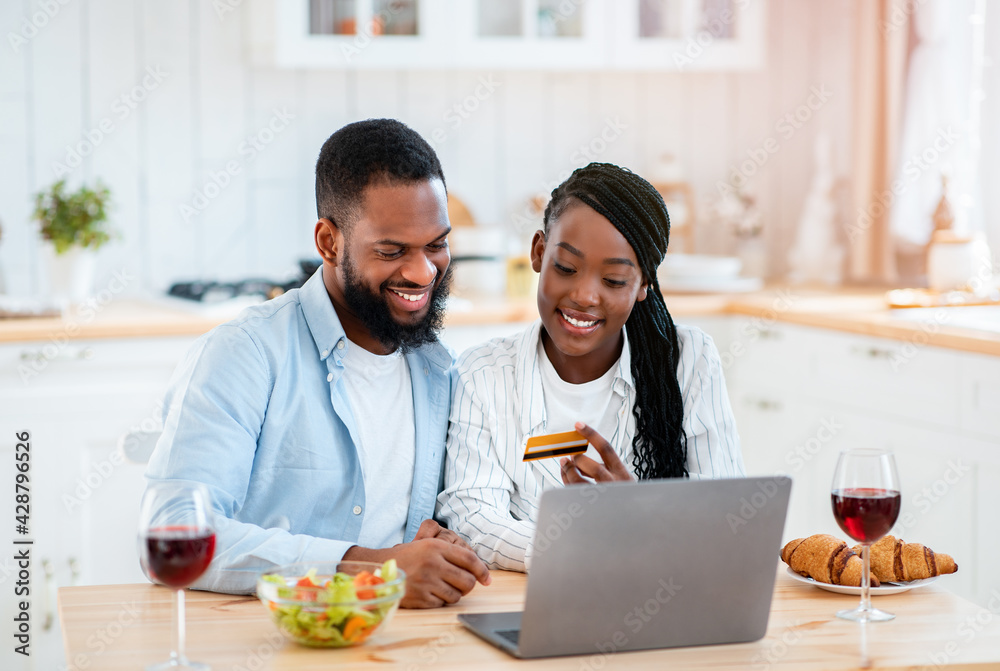 Black Couple Making Online Shopping With Laptop And Credit Card In Kitchen Black Couple Making Online Shopping With Laptop And Credit Card In Kitchen