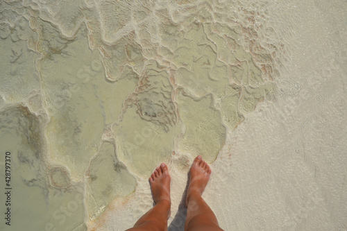Women foots on Pamukkale Hot Springs close-up texture, detail of travertine cascades  background. Abstract texture of salt mineral springs