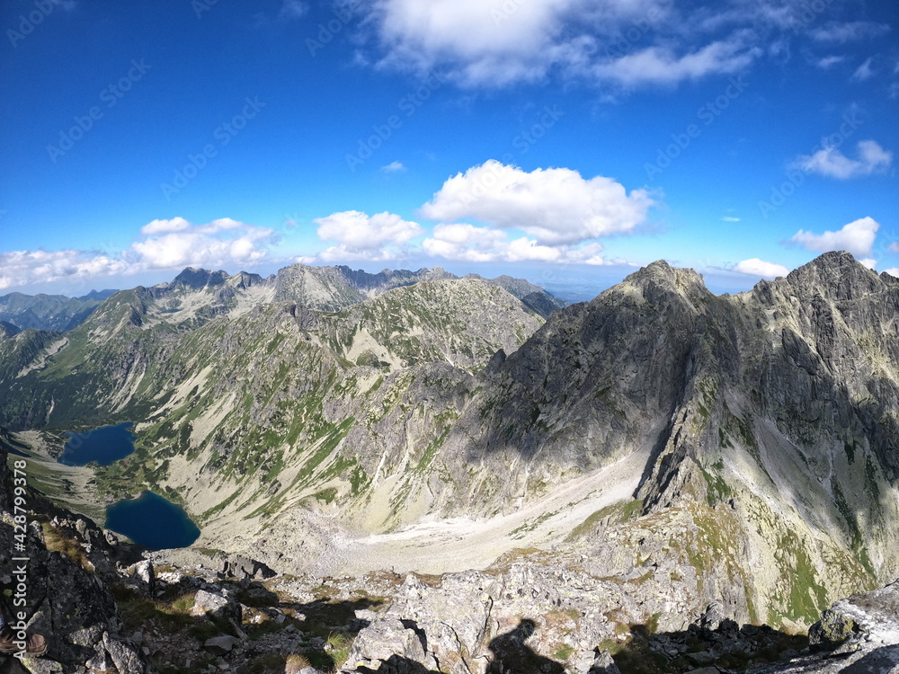 Enormous mountain side towering over small lakes located beneath rocky mountain peak, in the middle of the mountains.