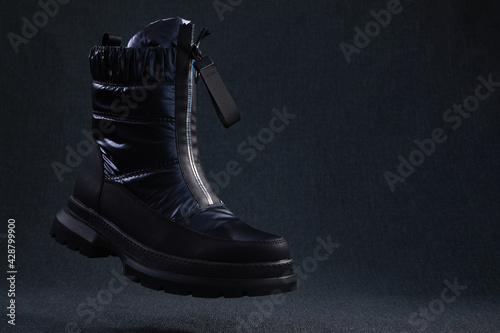 Fashion black unbranded boot flying on dark background. Black winter walking shoes levitate in air. Modern stylish female shoes for off-road walking.