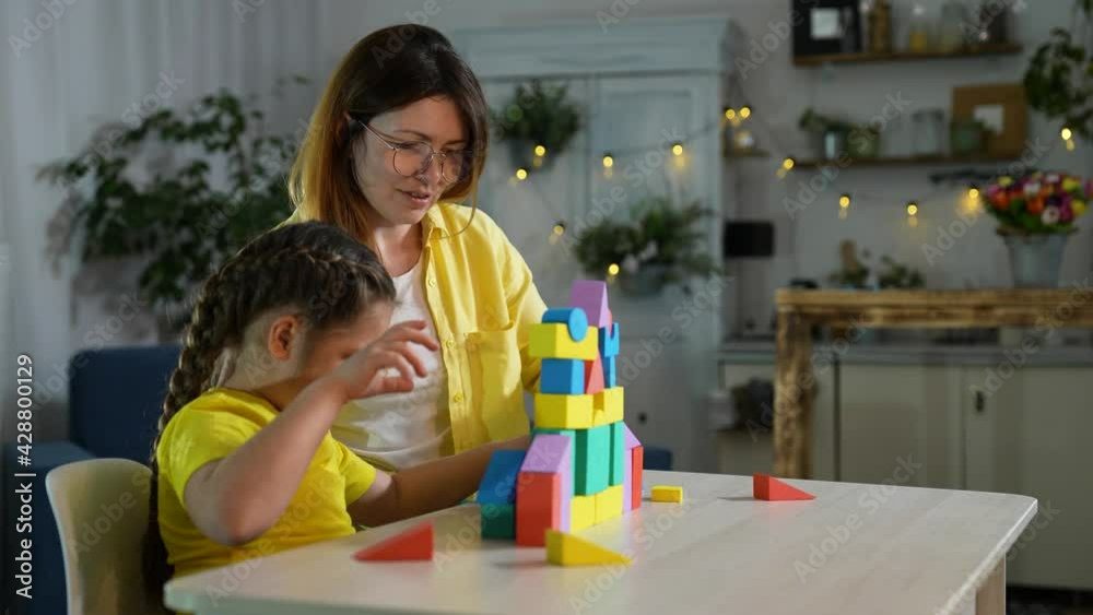 Happy family. Mom and daughter are building house from construction set. Family teamwork concept. Happy daughter builds house from colored constructor. Happy family with color constructor. Teamwork Happy family. Mom and daughter are building house from construction set. Family teamwork concept. Happy daughter builds house from colored constructor. Happy family with color constructor. Teamwork