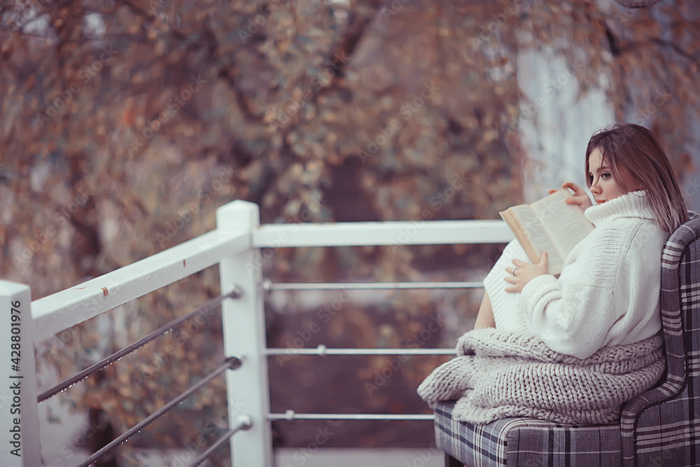 Fototapeta premium girl in a knitted sweater reads a book on the veranda in the park, seasonal romance concept