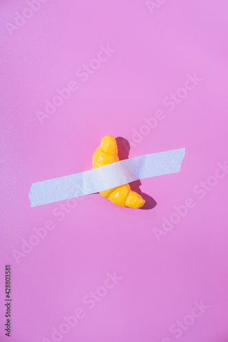 A French croissant or bun is glued with white tape to a purple background. Creative fun concept in the style of minimalism.