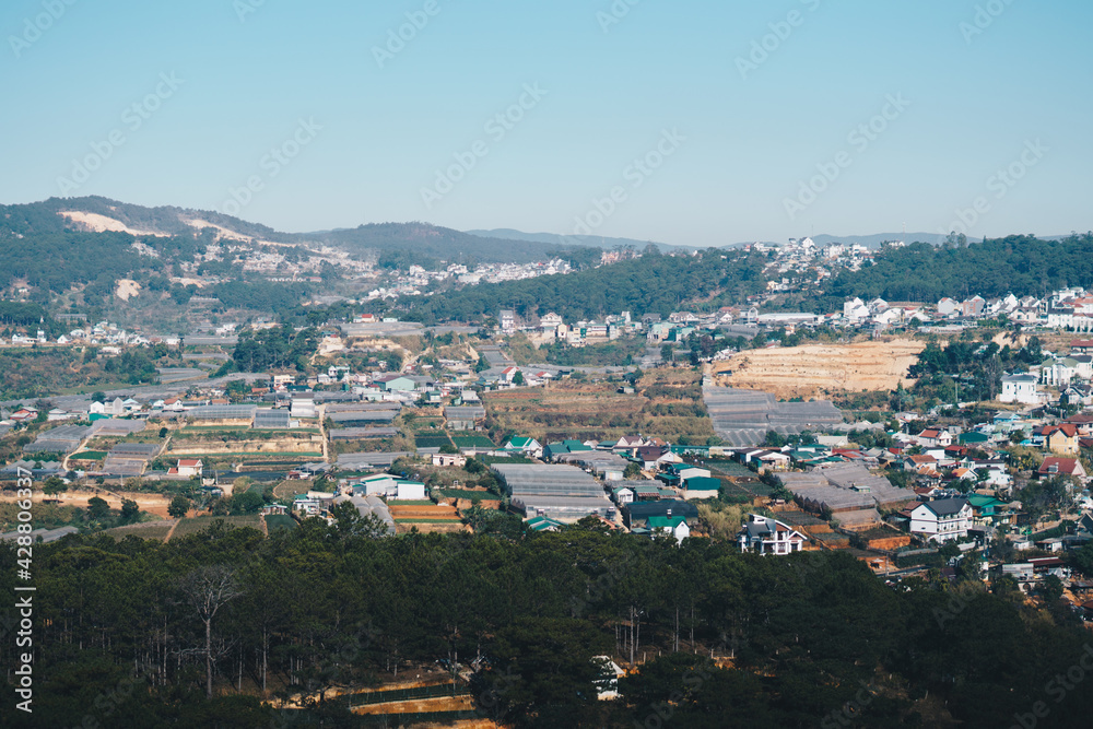 Panorama landscape, Dalat city, Langbian Plateau, Vietnam Central Highland region. Vegetable fields, many houses, architecture, farmlands, greenhouses. Forested Mountain background. Evening photo