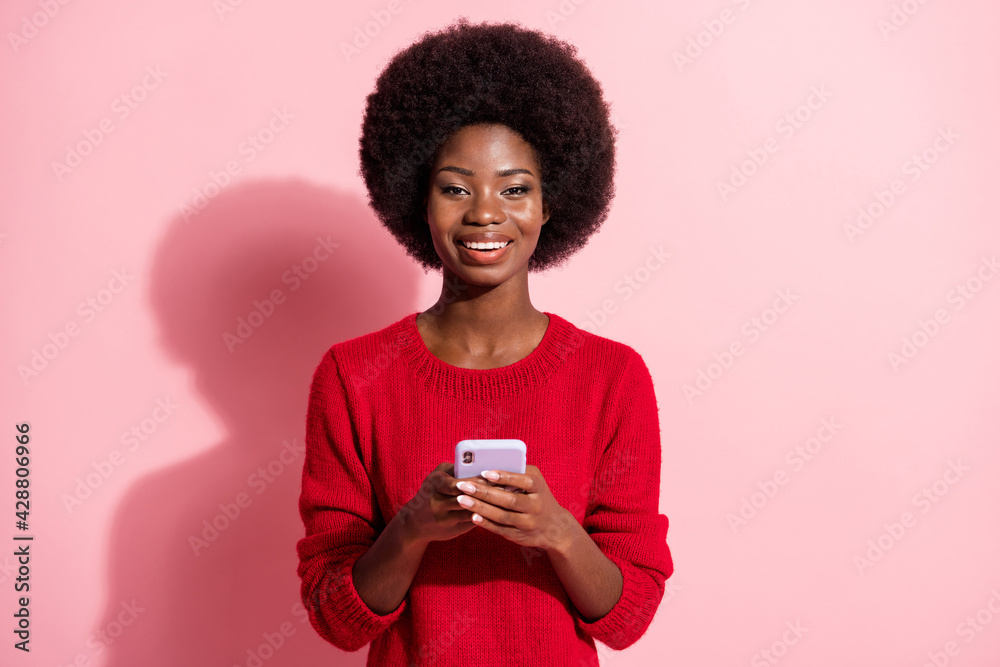Photo of dark skin charming attractive woman hold smartphone smile isolated on pastel pink color background Photo of dark skin charming attractive woman hold smartphone smile isolated on pastel pink color background