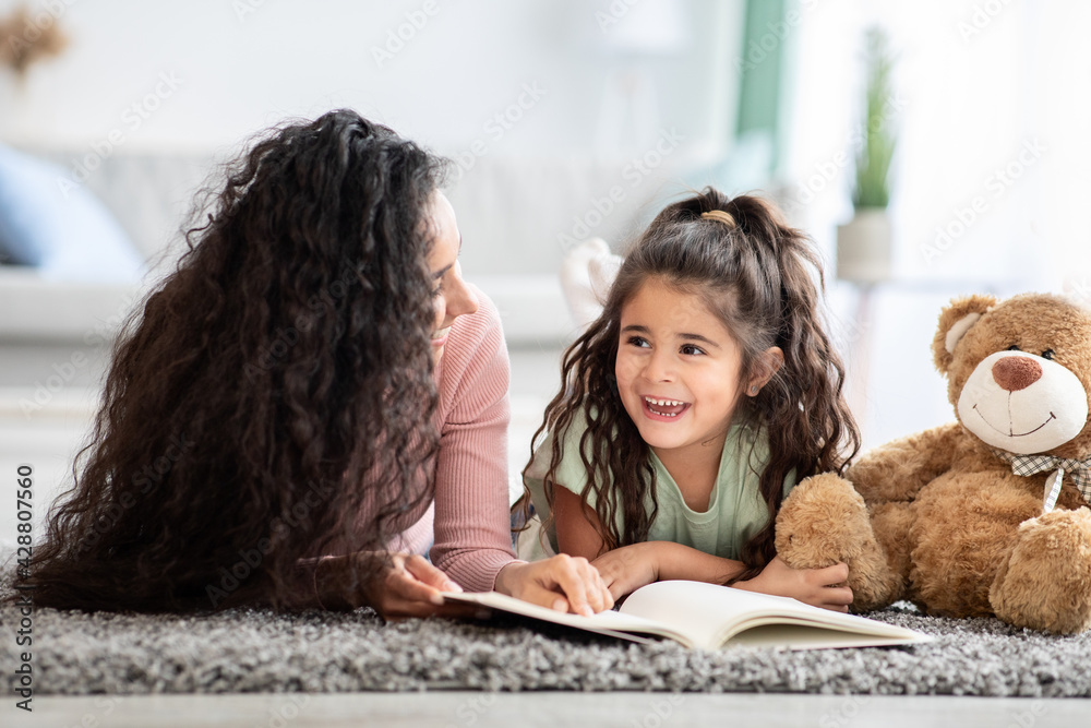 Loving young mother and her cute little daughter reading book at home Loving young mother and her cute little daughter reading book at home