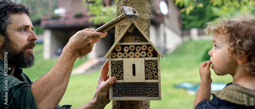 Small girl with father holding bug and insect hotel in garden, sustainable lifestyle. © Halfpoint