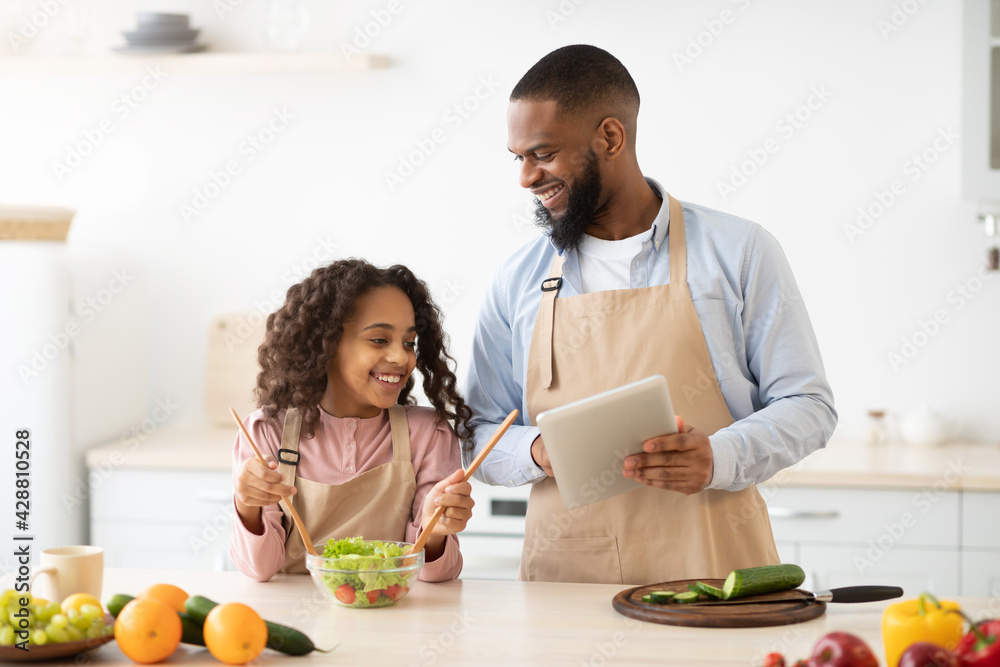 Black man and girl cooking in the kitchen using tablet