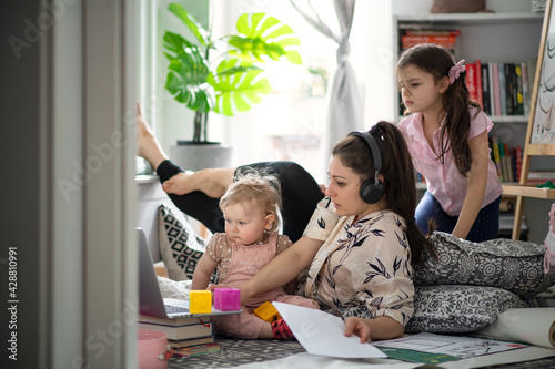 Mother working with small daughters in bedroom, home office concept.