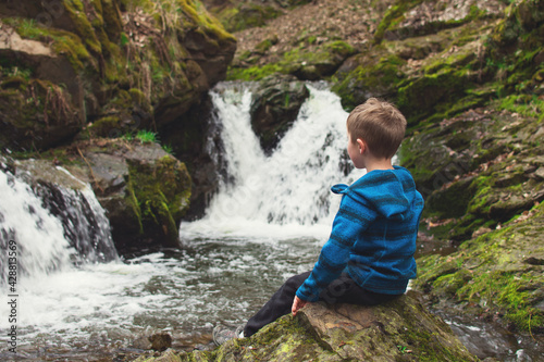 Kid sitting on the rock and looking at waterfall on the river in the rocks. Tourism with children concept.