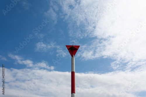 red and white pillar with a red triangular sign and a blue cloudy sky in the background photo