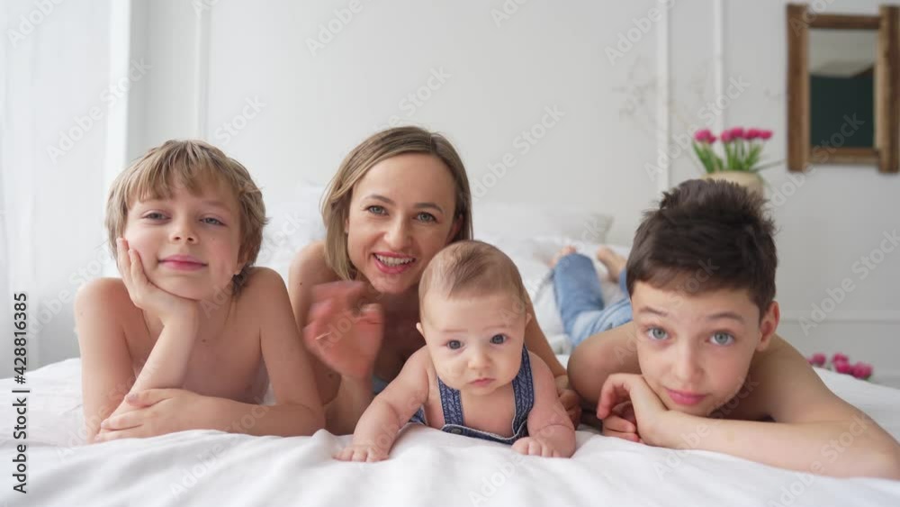 Mom and three sons are having fun on a white bed. Happy family concept. High quality 4k footage Mom and three sons are having fun on a white bed. Happy family concept. High quality 4k footage