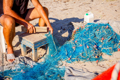 Fisherman cleans the fishing net, breaks the shells © Roman_23203