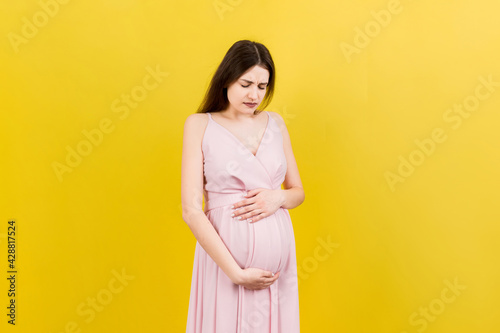 a pregnant girl who has a stomach ache stands on a colored background. isolated