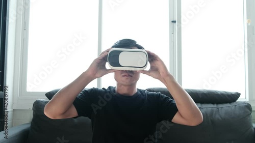Virtual reality putting on VR headset immerse within the function Asian man interacting waving hands making gesture in augmented reality using virtual user interface UI futuristic technology at home
