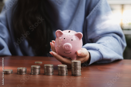 Woman hand holding piggy bank on wood table. Save money and financial investment.