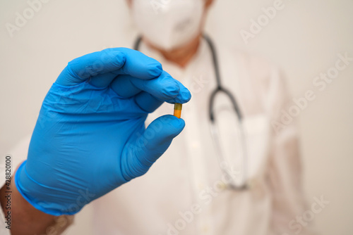 A doctor's hand in a blue latex glove holds a medical pill.