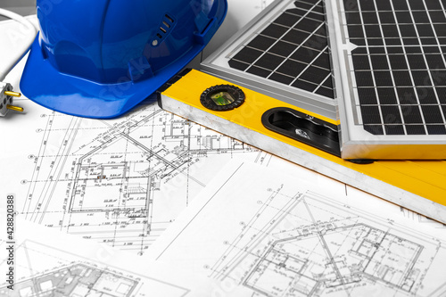 Construction blueprints, hardhat and solar battery on architect's table