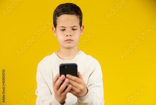 Cute boy using mobile phone isolated over yellow background. © Danko