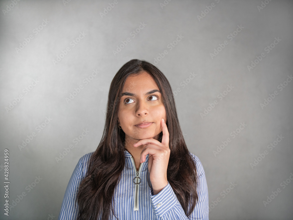 Close-up of a brown-haired woman's face in a blue striped jersey. Facial expression, questingly, in thought and doubts. The chin on her finger, the eyes looks upward at a green background.