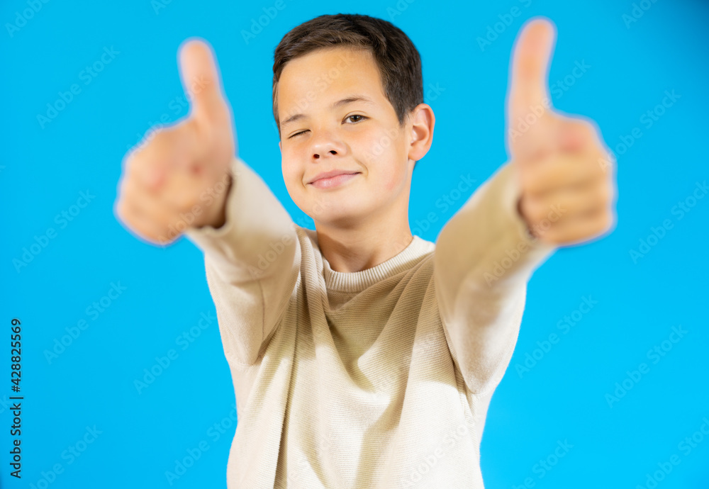 Smiling boy in casual sweater showing thumbs up isolated over blue background. Smiling boy in casual sweater showing thumbs up isolated over blue background.