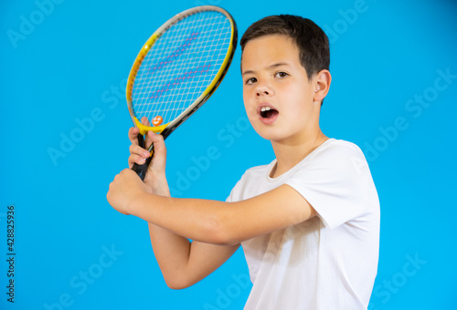 Young boy with tennis racket isolated over blue background.
