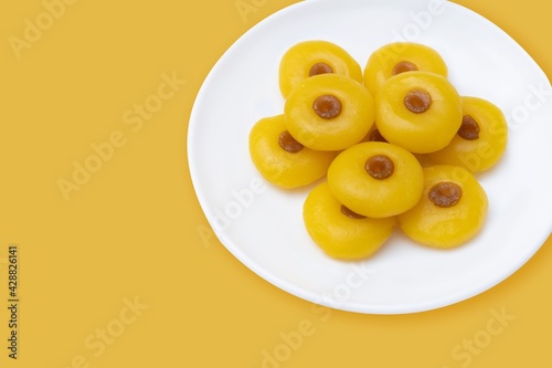 Kanom Sanay Chan, traditional sweet dessert originating in Thailand - Nutmeg –like yellow sweetmeats, serving on white plate isolated on yellow photo