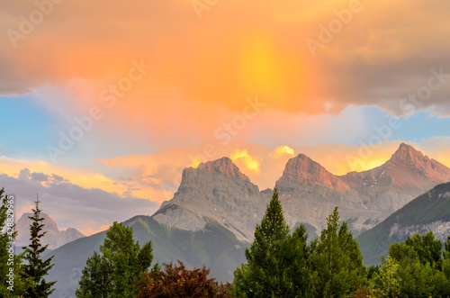 Scenery of high mountain peaks over stormy sky with white clouds and orange (yellow) glowing effect.