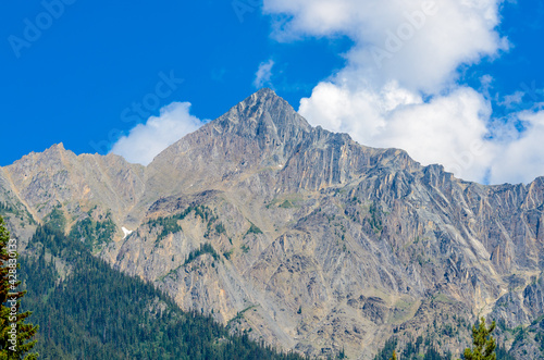 Scenery of high mountain peak over blue sky with white clouds.