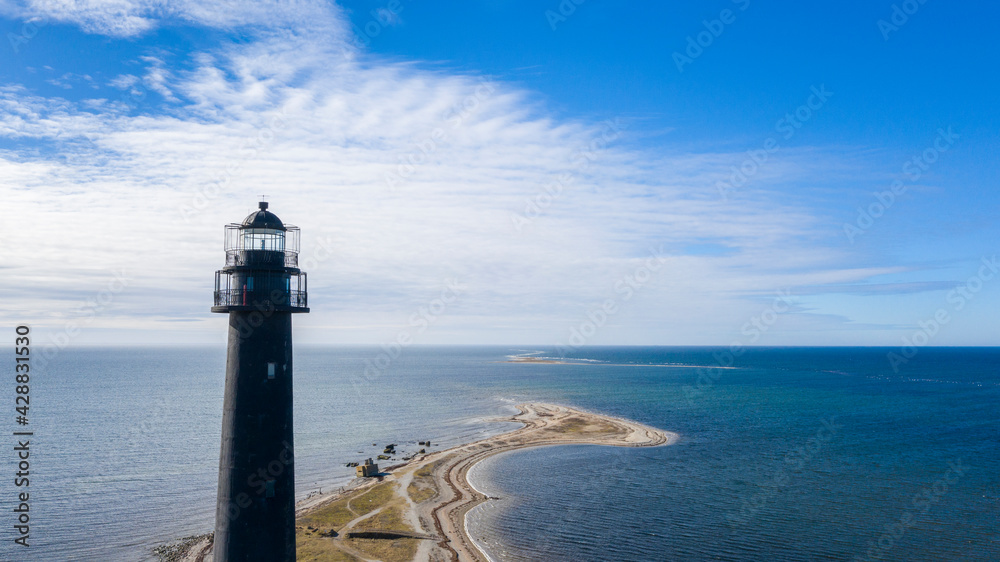 Aerial view to the historic lighthouse on on the daytime seascape with the long spit submerging into deep blue sea