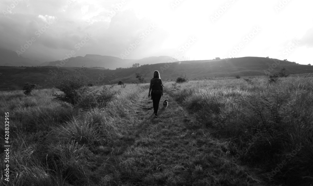Woman and dog hiking in the mountains on a path in black and white

