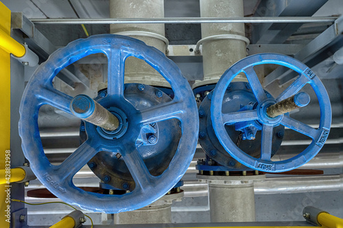 Two blue valves with valve control wheel with part of pipeline in the control room