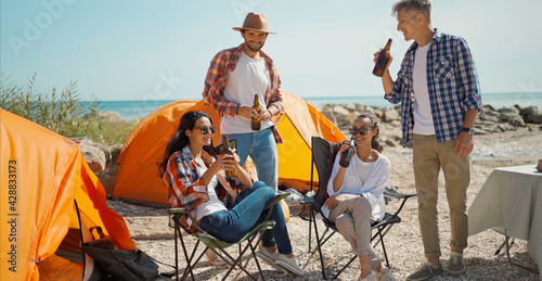 friends drinking cold beer at hot sunny day in camping, having fun during weekend