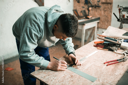 Portrait of a real tinsmith blacksmith of a man who works with metal in his workshop, makes measurements with a ruler Portrait of a profession.