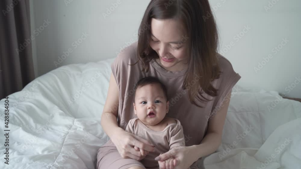 asian mother parent playing with baby infant holding hand and singing a song. kid laughing when play with mom on bed in bedroom. life at home. happy newborn baby learning development skill lesson. asian mother parent playing with baby infant holding hand and singing a song. kid laughing when play with mom on bed in bedroom. life at home. happy newborn baby learning development skill lesson.